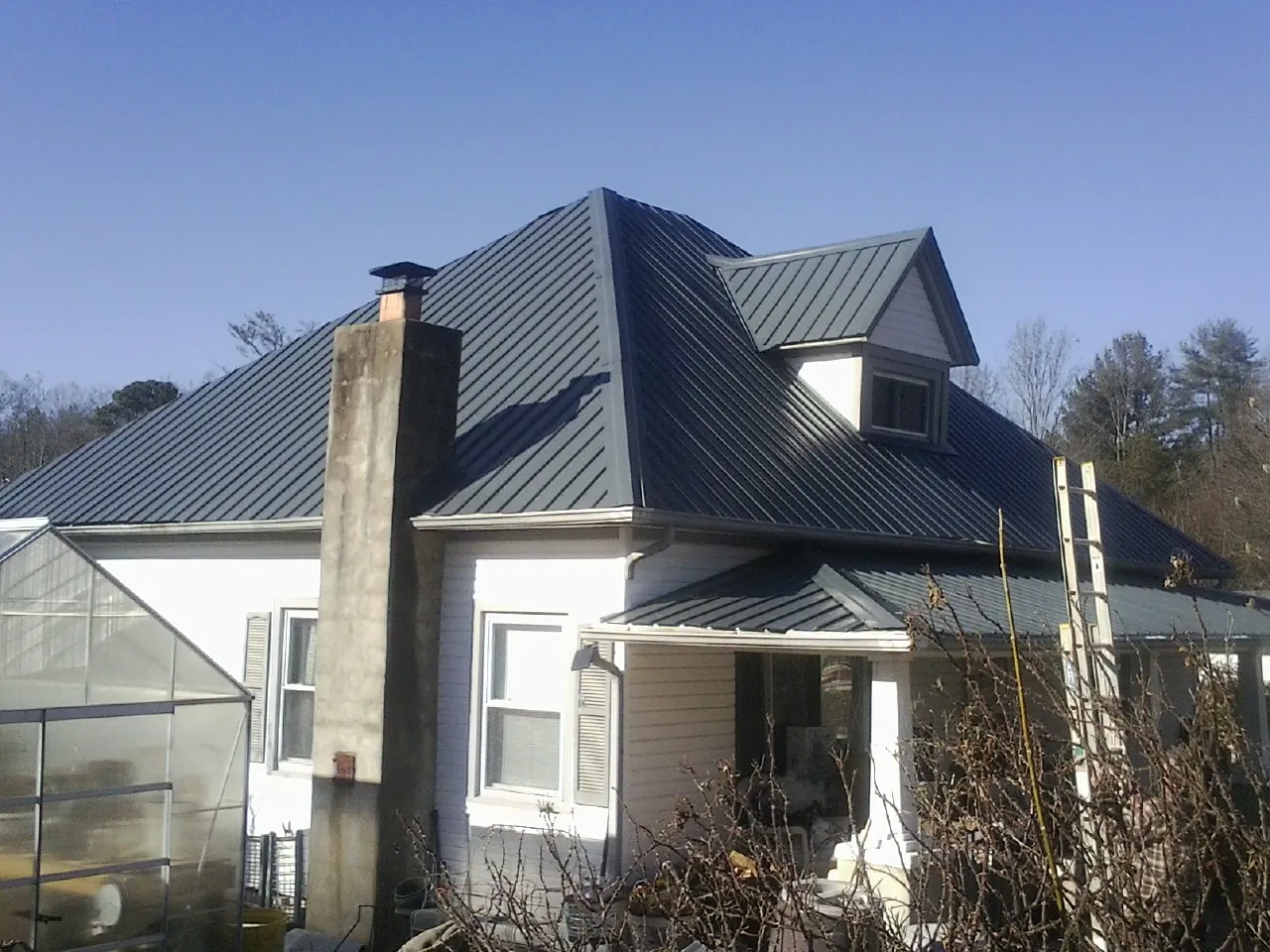 Dark blue standing seam metal roof on a white farmhouse with dormer — Slate & Tile Roof Repair by Roofing Brothers in Mabel