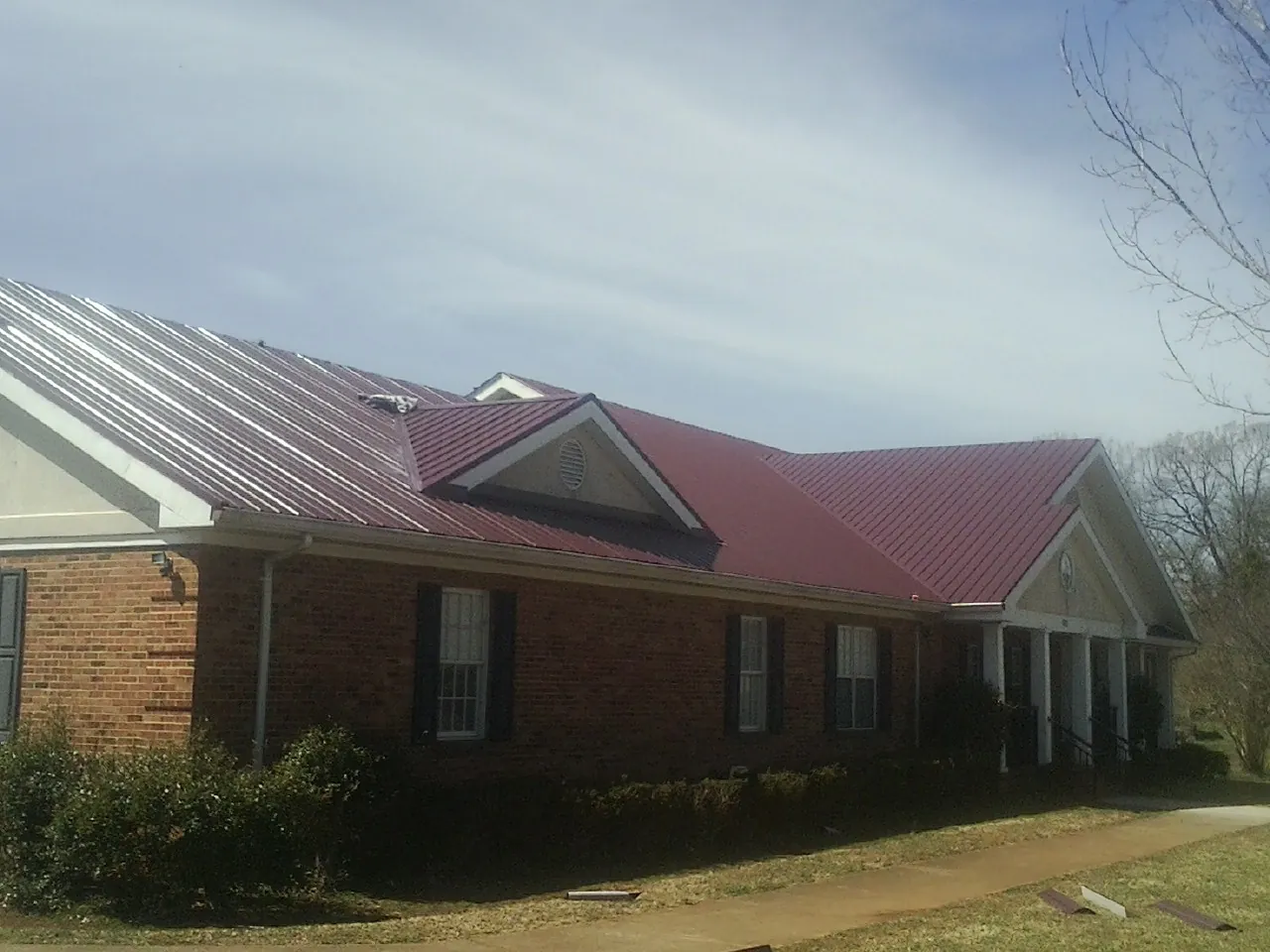 Red metal roof with gabled entries on a long brick building, from a Hail Damage Roof Repair job in Mabel