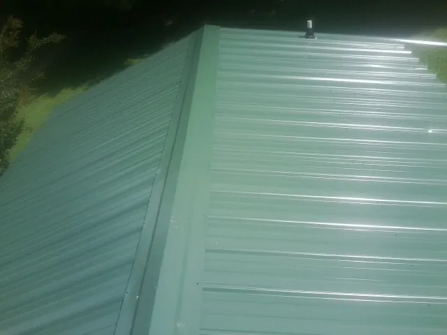 New green metal panels meeting at the ridge of a roof — Flat Roof Repair work by our crew in Mabel