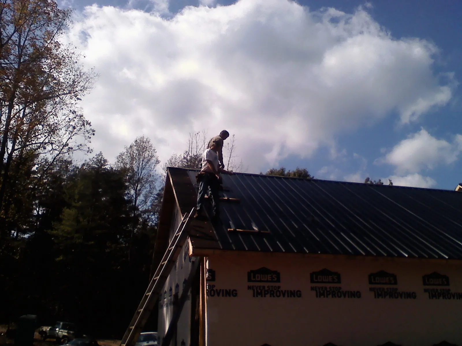 Roofer fastening dark metal panels high against a cloudy sky, from a Roof Inspection job in Mabel